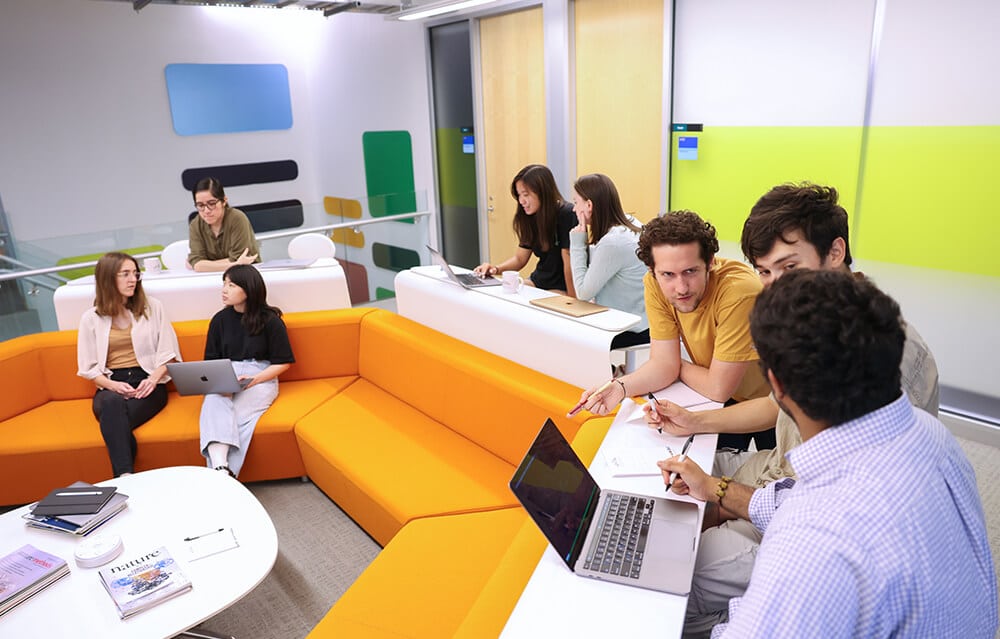 A group of colleagues socialize in the common area with brightly colored seating at NYGC